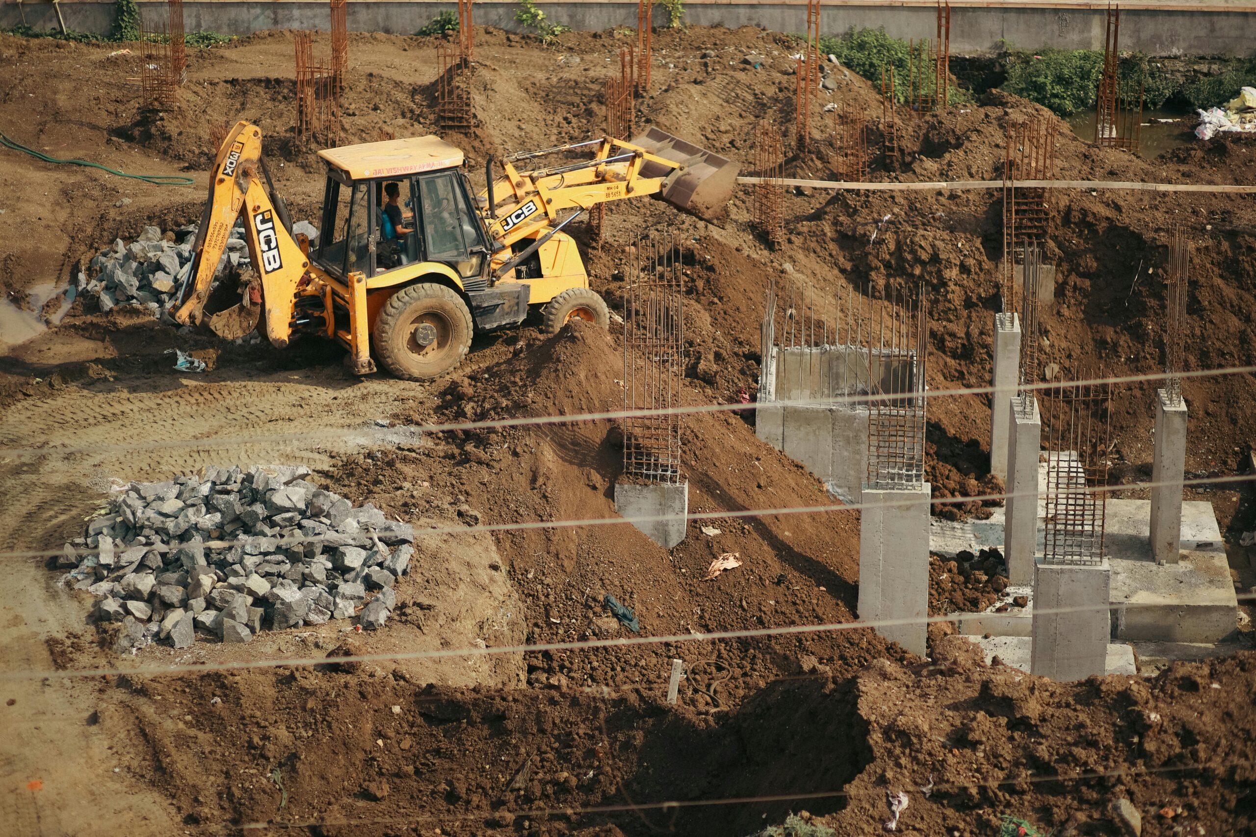 Jem Prime Limited Services. A bulldozer moves soil at a busy construction site, surrounded by piles of gravel and concrete structures.