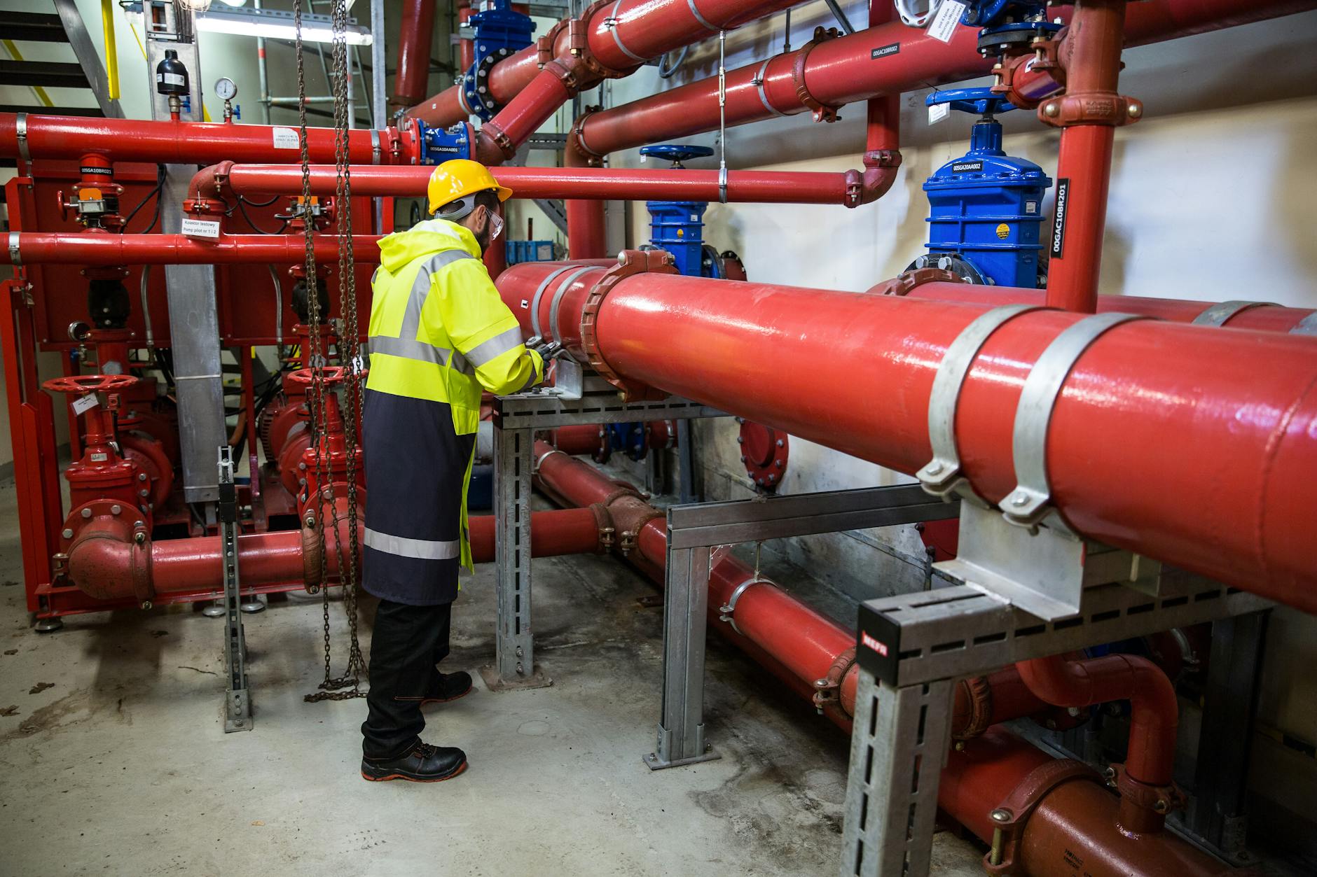 Jem Prime Limited Services. Engineer with safety gear inspecting red industrial piping system indoors.