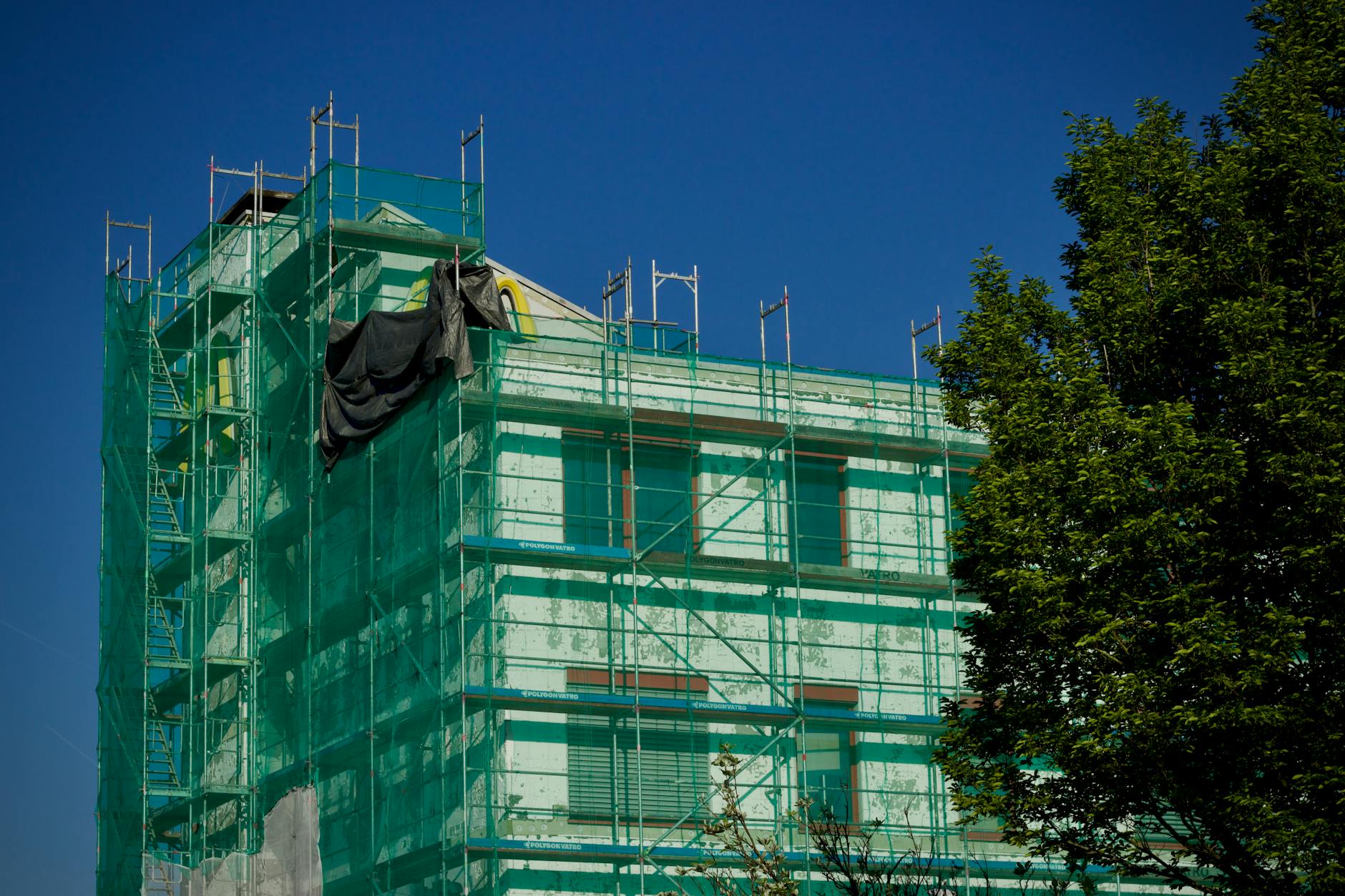 Jem Prime Limited Services. Building under renovation covered with green scaffolding against a clear blue sky.